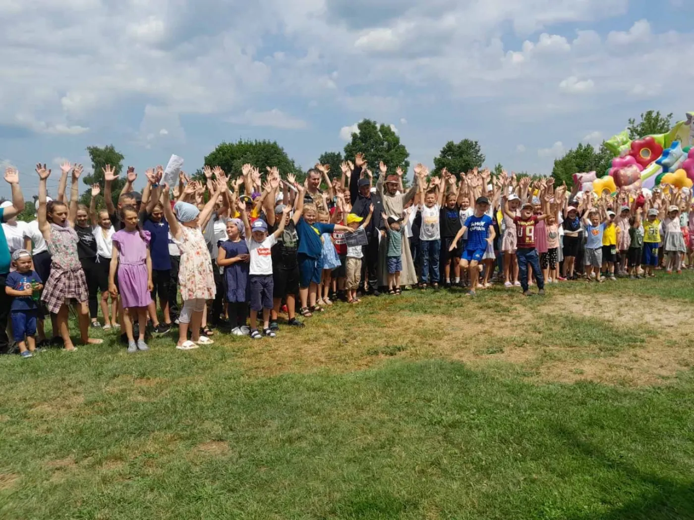 Des dizaines d'enfants de Bérezné lèvent les bras et sourient lors d'une fête en plein air